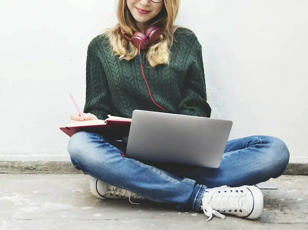 a young woman with laptop writing down the notes
