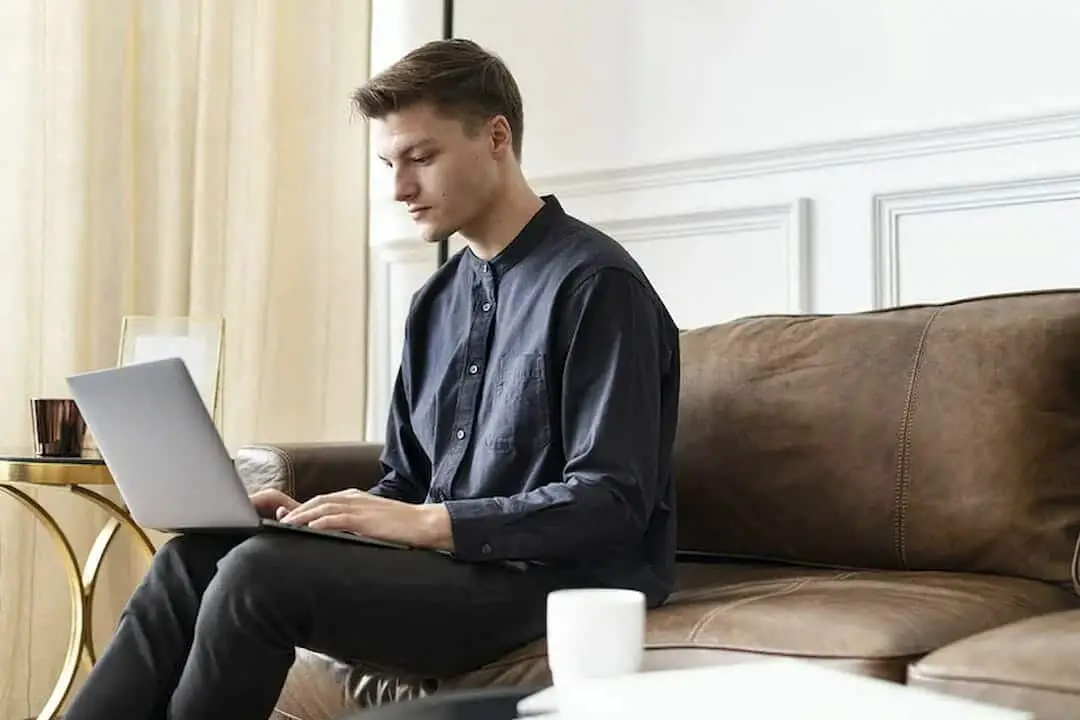 a young man sitting on the couch and typing on the laptop 